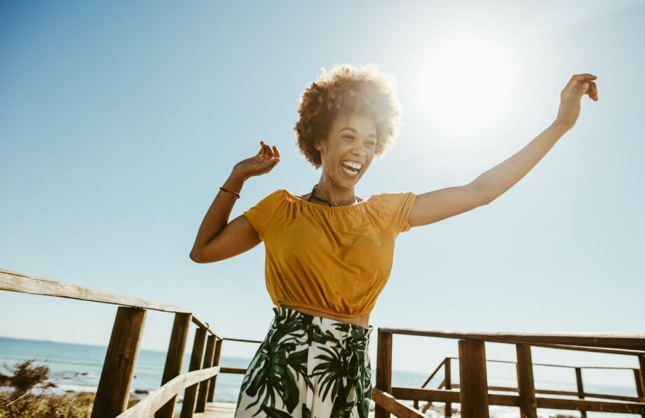 Happy woman with short, dark hair smiling outdoors while the sun shines in the background.