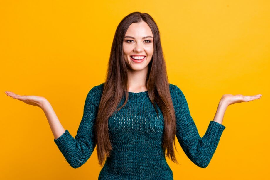 Close up photograph of a woman with long, straight brown hair with both her hands up as if she was weighing out her options.