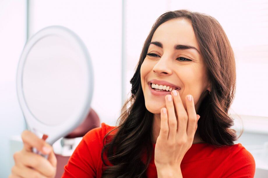 Woman looking at her teeth in a hand mirror